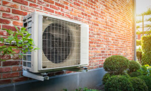 Side view of outdoor energy unit hanging on brick wall of house on a sunny day.