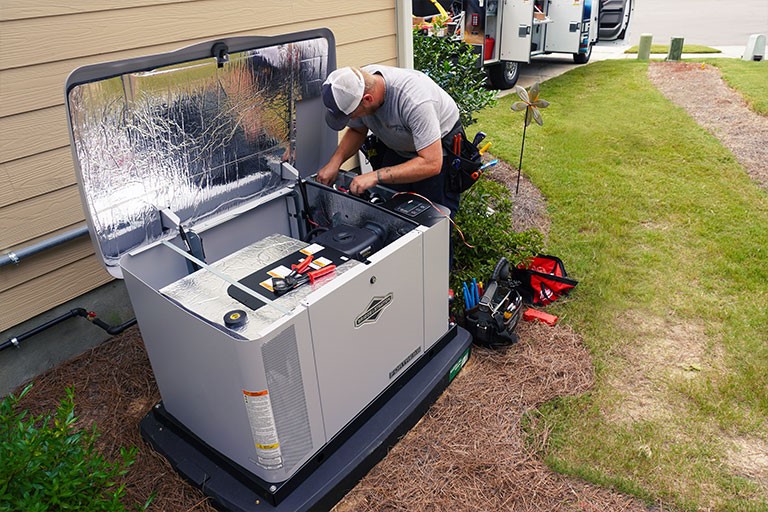 Technician repairing a whole-home generator outside a tan home.
