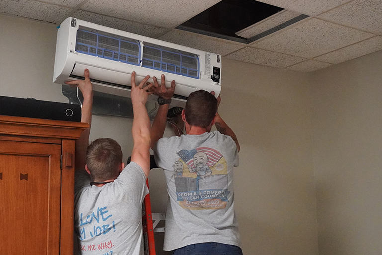 Two technicians installing a ductless mini-split air handler in a home