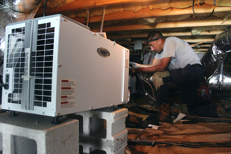 HVAC technician installing a dehumidifier in a crawl space