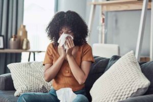 A woman sneezing into a tissue at home because of spring allergies
