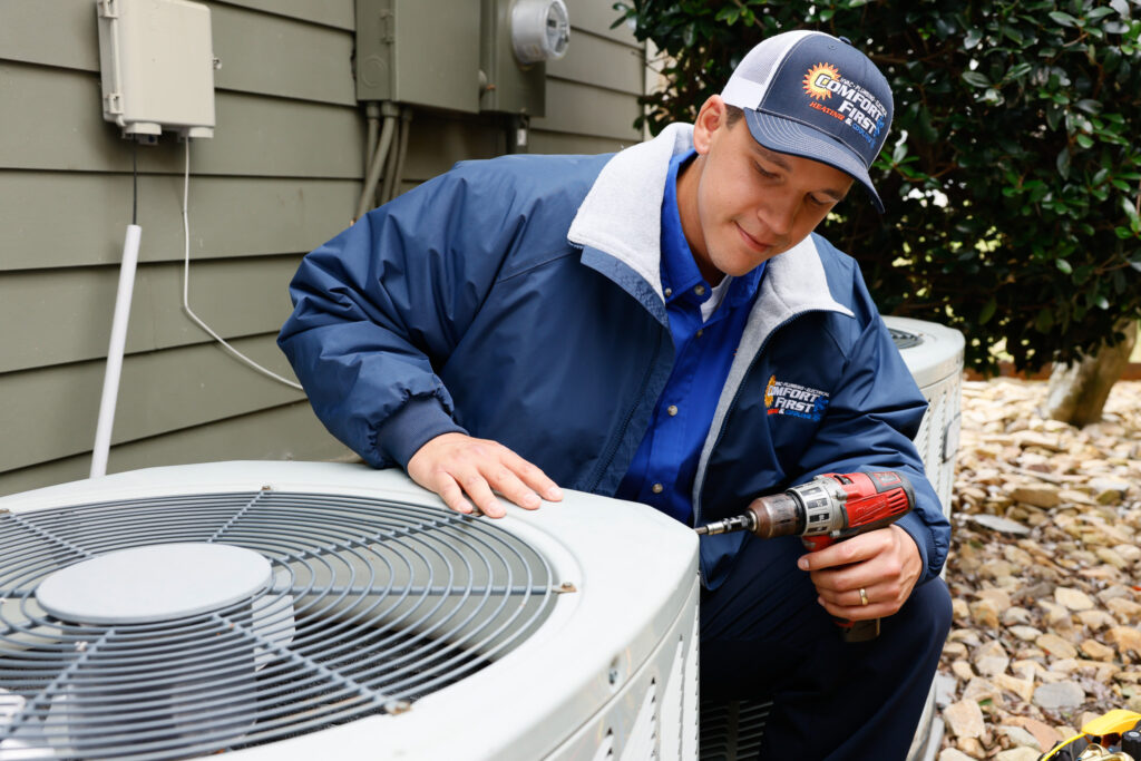 Technician repairing an outdoor HVAC unit next to a home.