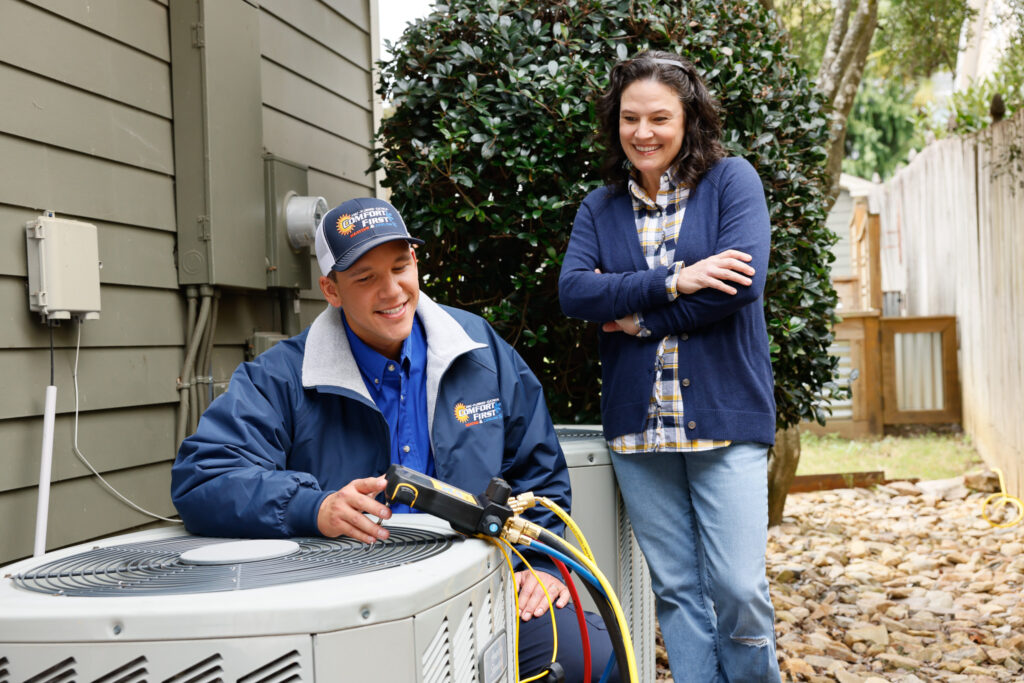 HVAC tech working on an ac unit with a woman watching