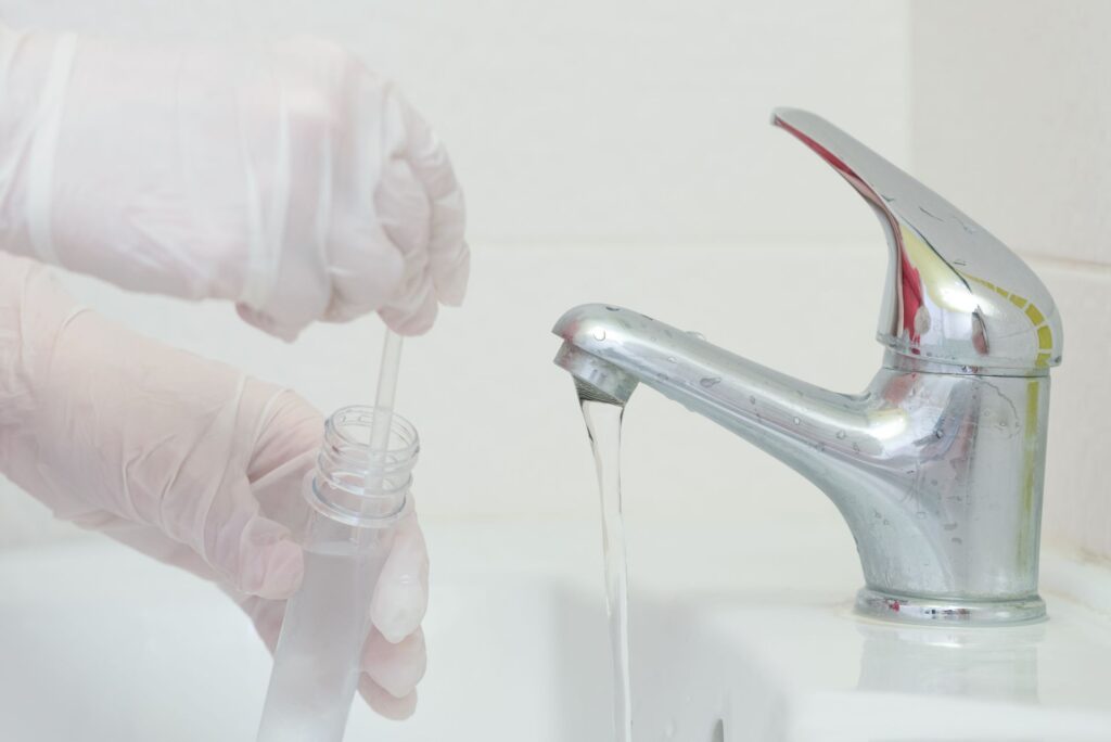 Glove hand holding test tube and taking a water sample from a bathroom sink