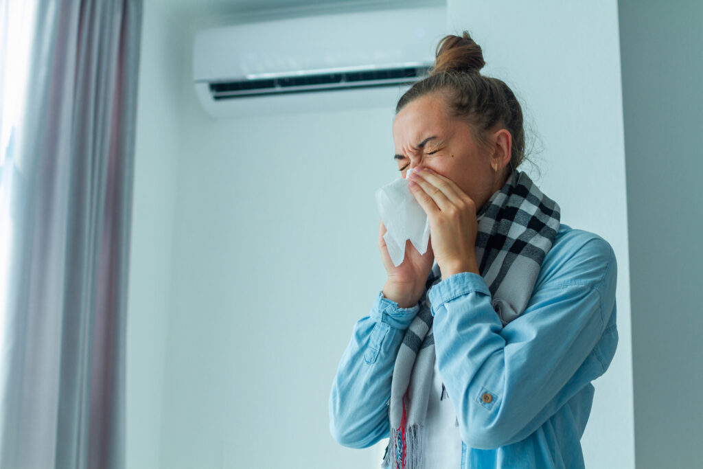 Sick sneezing woman in front of a ductless-mini-split